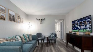 A living room with a blue sofa, two grey armchairs, a coffee table, a TV on a wooden stand, and a bull skull decoration on the wall. - Lux Modern Getaway At&t Stadium Views King Bed (Arlington)