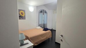 A room with a bed, a lamp, a painting, a door, and a towel rack. - Apartment in Villa Gra&Mary (Tombaccia)