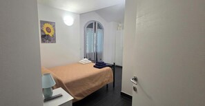Ein Zimmer mit einem Bett, einer Lampe, einem Bild, einer Tür und einem Handtuchhalter.