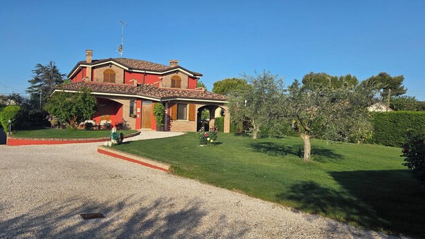 A two-story house with a red facade, a gravel driveway, and a well-maintained lawn. - Apartment in Villa Gra&Mary (Tombaccia)