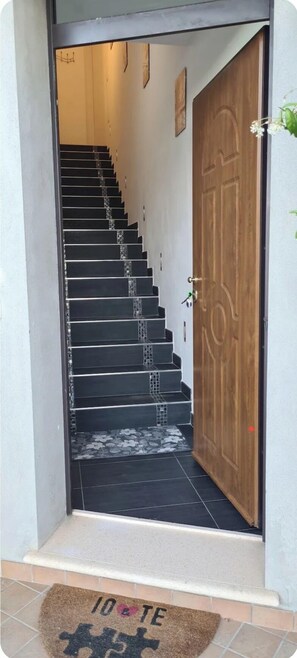 Eine Treppe führt zu einer Holztür, eine Fußmatte mit Puzzle-Muster und ein Fliesenboden.