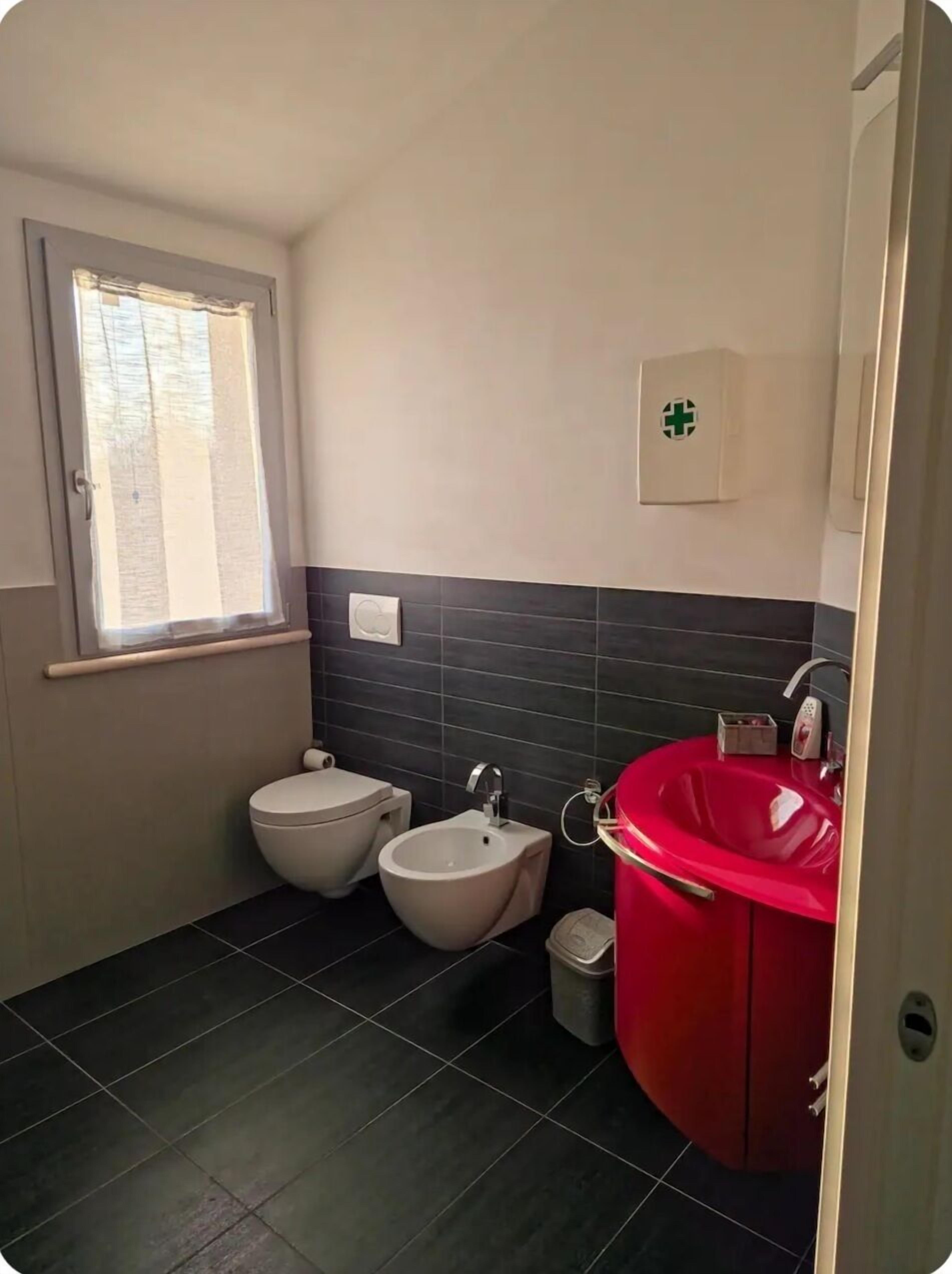 Ein Badezimmer mit Toilette, Bidet und einem roten Waschbecken.