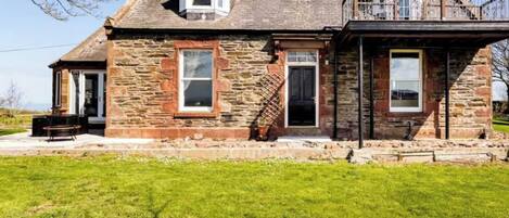 A stone house with a balcony, a front door, and a small attached shed.