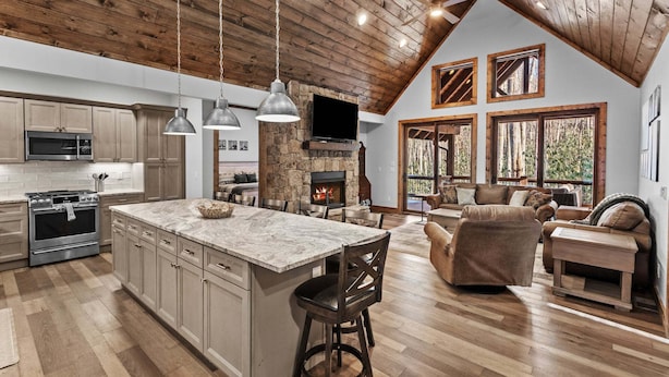 A spacious kitchen with a large island, a stone fireplace, and a cozy living area with a fireplace and comfortable seating. - The Cabins on Buckeye Creek at Eagles Nest (Banner Elk)