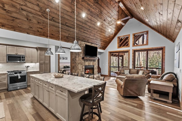 A spacious kitchen with a large island, a stone fireplace, and a cozy living area with a fireplace and comfortable seating. - The Cabins on Buckeye Creek at Eagles Nest (Banner Elk)