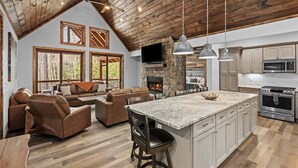 A spacious living area with a stone fireplace, wooden ceiling, and a large kitchen with modern appliances. - The Cabins on Buckeye Creek at Eagles Nest (Banner Elk)