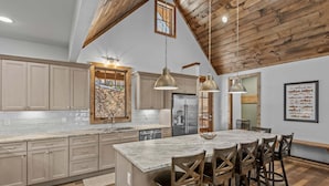 A spacious kitchen with wooden beams, a large island, and pendant lighting. - The Cabins on Buckeye Creek at Eagles Nest (Banner Elk)