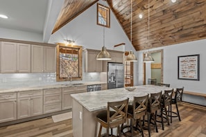 A spacious kitchen with wooden beams, a large island, and pendant lighting. - The Cabins on Buckeye Creek at Eagles Nest (Banner Elk)
