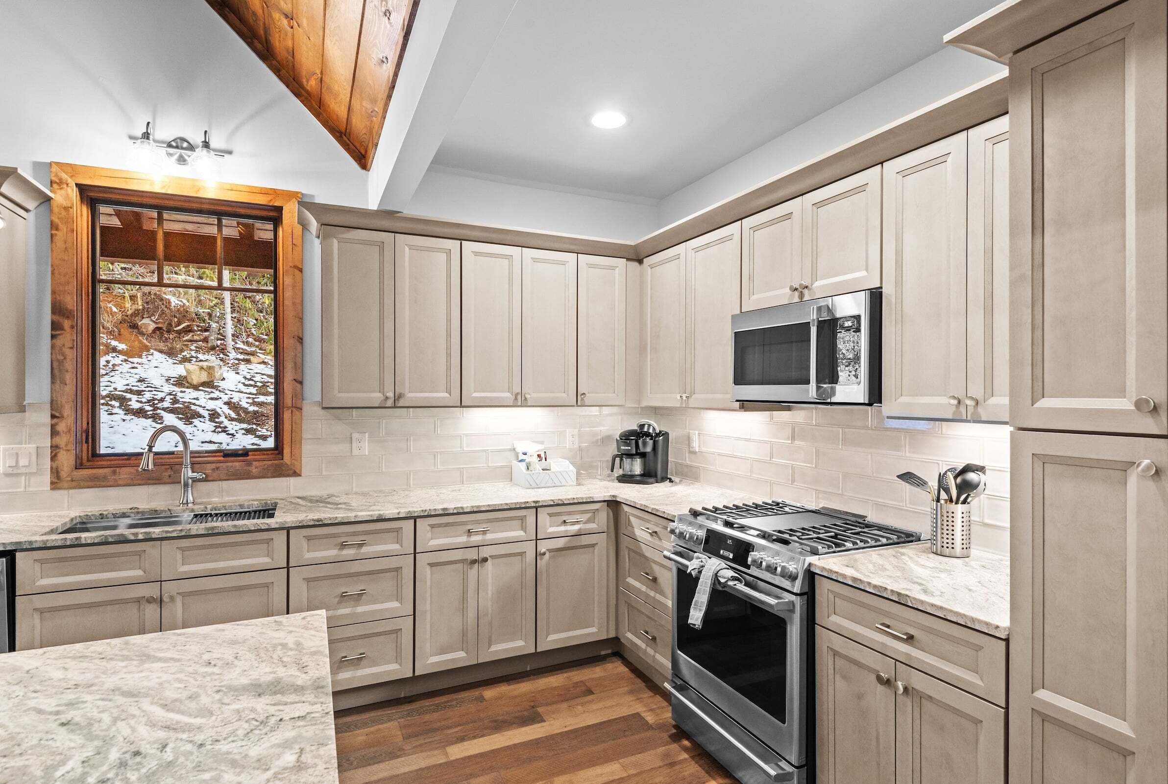 A kitchen with wooden cabinets, a stove, a microwave, and a window with a view of snow.