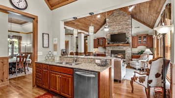 A spacious kitchen with granite countertops, a built-in dishwasher, wooden cabinets, and a stone fireplace.