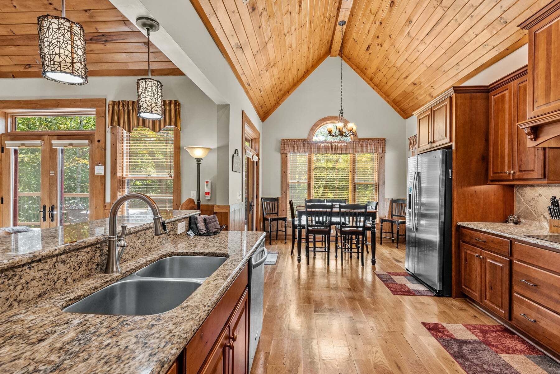 A spacious kitchen with granite countertops, stainless steel appliances, wooden cabinets, and a high ceiling with exposed beams.