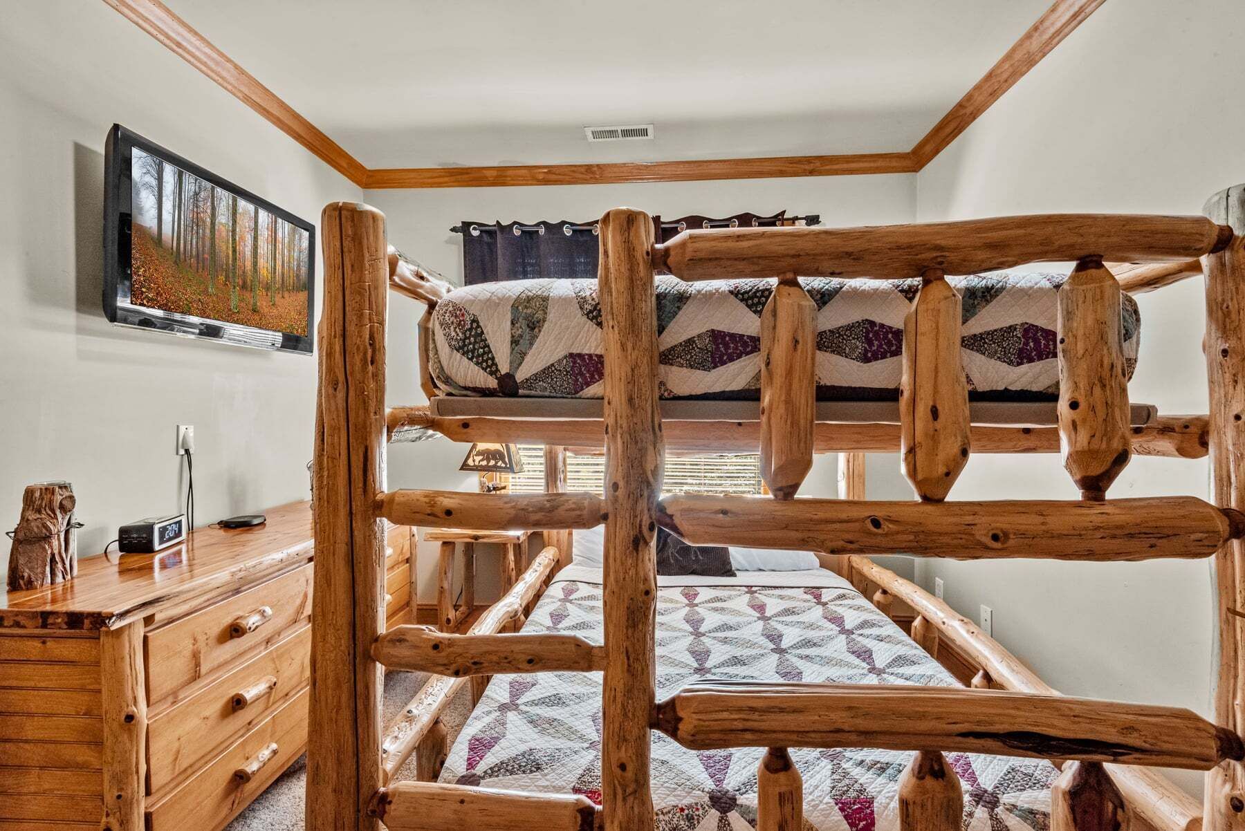 Un lit superposé avec une structure en bois, un bureau avec des tiroirs, une horloge et un tableau accroché au mur.