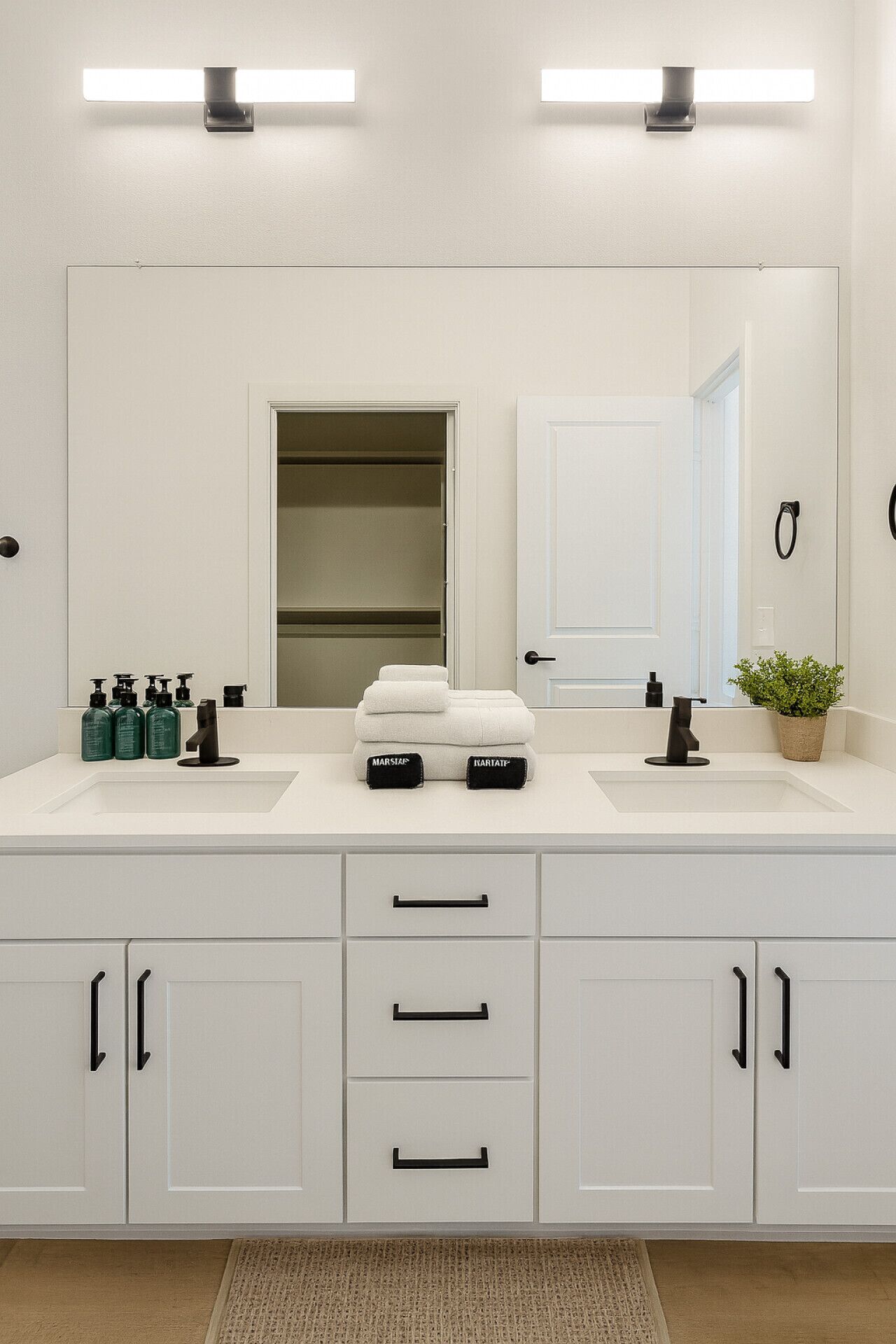 A modern bathroom with two sinks, a large mirror, and a walk-in closet.