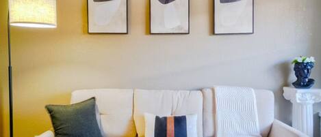 Uma sala de estar moderna com um sofá, três quadros abstratos emoldurados, um abajur e um vaso com flores.