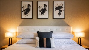 A hotel room with a large bed, white bedding, a tufted headboard, and three black-and-white abstract paintings on the wall. - King Suite - 10 min to Ft Moore (Columbus)