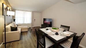 A compact living space with a dining area, a sofa, a TV, and a small table set for a meal. - King Suite - 10 min to Ft Moore (Columbus)