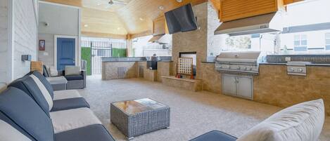 A spacious outdoor living area with a built-in grill, seating, and a television mounted on the wall.