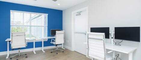 A modern office space with two desks, chairs, a ceiling fan, and a large window.
