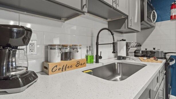 Una cocina moderna con gabinetes blancos, un lavamanos de acero inoxidable, una barra de café y una cafetera.