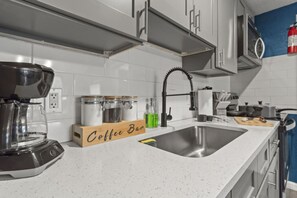 A modern kitchen with white cabinetry, a stainless steel sink, a coffee bar, and a coffee maker. - Cozy King Suite, Wheelchair Accessible, Fast Wifi (Columbus)