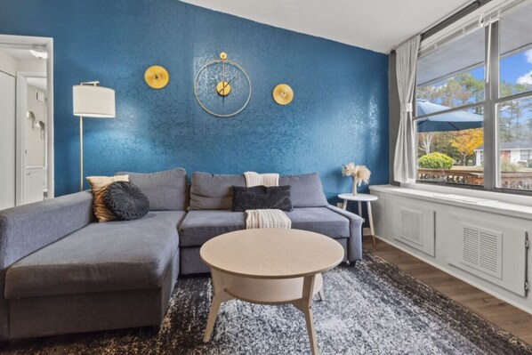 Una sala de estar con pared azul, un sofá seccional gris, una mesita de centro redonda y una mesita auxiliar pequeña.