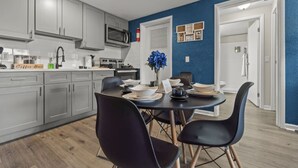 Una cocina moderna con armarios grises, un microondas y un letrero que indica 'Coffee Bar'. Hay una mesa de comedor con sillas negras y un jarrón con flores azules.