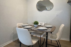 A dining area with a table set for four, white chairs, a small potted plant, and a wall-mounted mirror. - 2713 Kathrynln2 Plano 1BR (Plano)