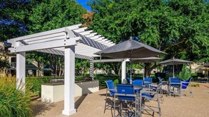 An outdoor patio area with white pergolas, blue chairs, and umbrellas. - 2713 Kathrynln2 Plano 1BR (Plano)