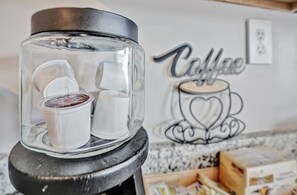 A coffee machine with a clear container and disposable cups, a wall with a coffee-themed artwork, and a countertop with boxes and a basket. - Legacy Executive Retreat (Clarksville)