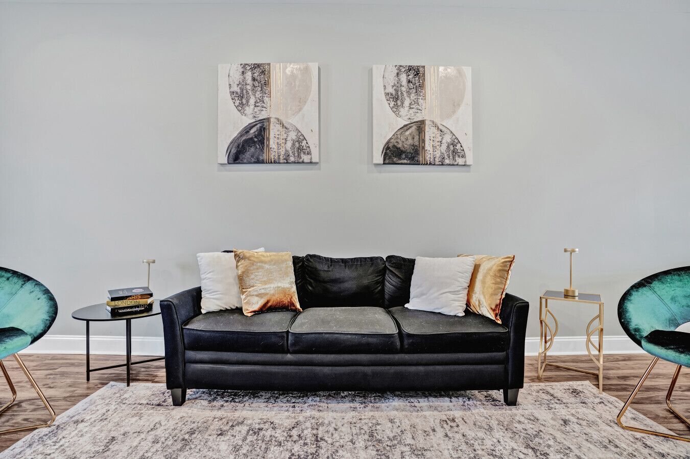 Un salon moderne avec un canapé noir, deux tables d’appoint et des fauteuils de couleur turquoise.