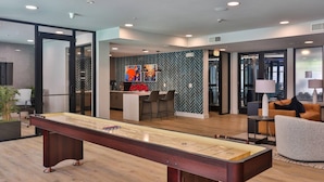 Un salon moderne doté d’une table de jeu de « shuffleboard », d’un coin cuisine avec un dosseret en motif chevrons et d’un espace détente comprenant un canapé et des fauteuils.