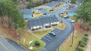 An aerial view of a motel with multiple rooms, a parking lot, and a small swimming pool. - King Suite, 10 Mins to Ft Moore (Columbus)