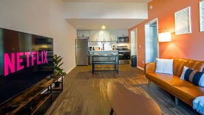 A modern living room with a TV, a sofa, and a kitchen in the background. - King Suite, 10 Mins to Ft Moore (Columbus)