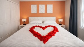 A hotel room with a large bed, white bedding, a heart-shaped decoration made of red flowers, two bedside lamps, and a window with curtains. - King Suite, 10 Mins to Ft Moore (Columbus)