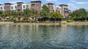 A waterfront hotel with modern architecture, a reflective water body, and a well-maintained garden area. - Stylish Modern Bedroomking Full Bed+pool&gym (Irving)