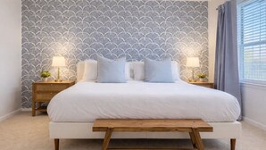 A bedroom with a bed, two bedside tables with lamps, a bench, and a patterned wallpaper. - 4113 Kathrynln2 Plano 2BR (Plano)