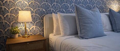 Une chambre à coucher avec un papier peint à motifs, une table de chevet avec une lampe et un lit avec des oreillers.