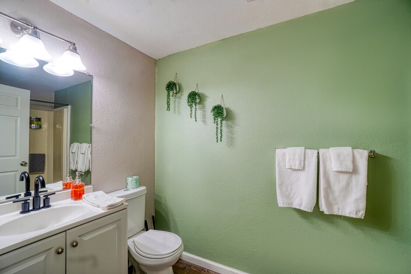 Un baño con un lavabo blanco, un inodoro y paredes verdes. Hay dos toallas blancas colgadas en la pared.