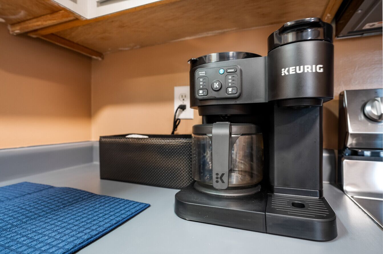 A Keurig coffee machine on a kitchen counter with a blue mat and a black basket.