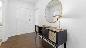Um corredor com uma mesa consola preta, um espelho redondo com moldura dourada e uma porta branca.