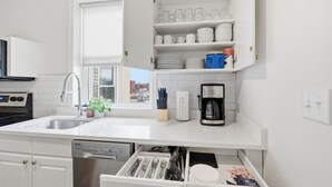 Cozinha moderna com armários brancos, lava-louças embutida, máquina de café e janela que oferece luz natural.