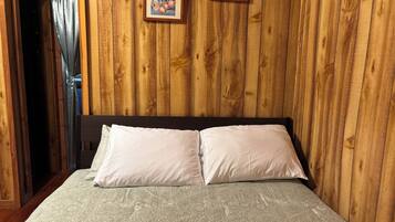 Una habitación con paneles de madera, una cama, dos cuadros en la pared y una cortina.