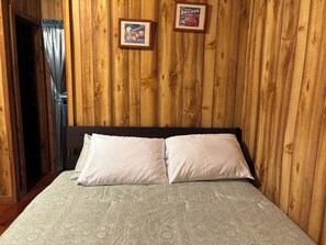 A wooden-paneled room with a bed, two framed pictures on the wall, and a curtain.