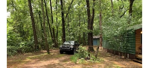 A forested area with a vehicle parked near a cabin. - Cozy 1-bedroom manufactured home with cabin vibe in adorable Glenwood with AC (Glenwood)