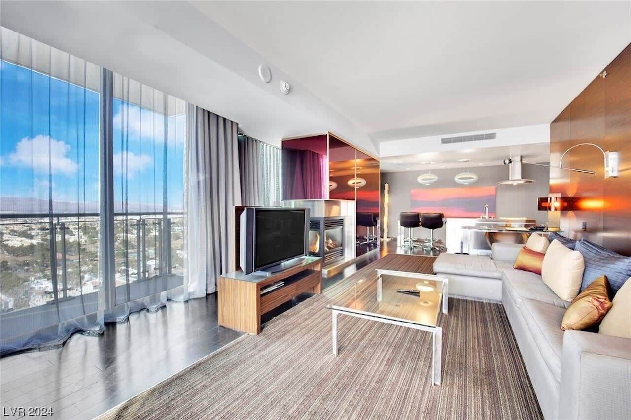 Una habitación de hotel moderna con un ventanal grande, televisor de pantalla plana, sofá, una mesita de centro y chimenea.