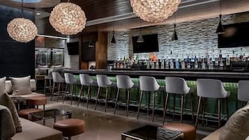 A modern bar area with round, textured hanging lights, a bar counter stocked with bottles, and a seating area with cushioned chairs and tables.