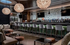 Een moderne barruimte met ronde, gestructureerde hanglampen, een bar met flessen en een zithoek met gestoffeerde stoelen en tafels.