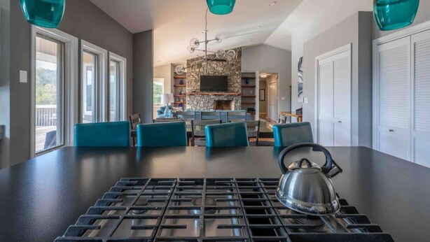 A modern kitchen with a gas stove, teal pendant lights, and a stone fireplace. - 550 Massive 4 Bedroom Home Sleeps 19 (Candler)