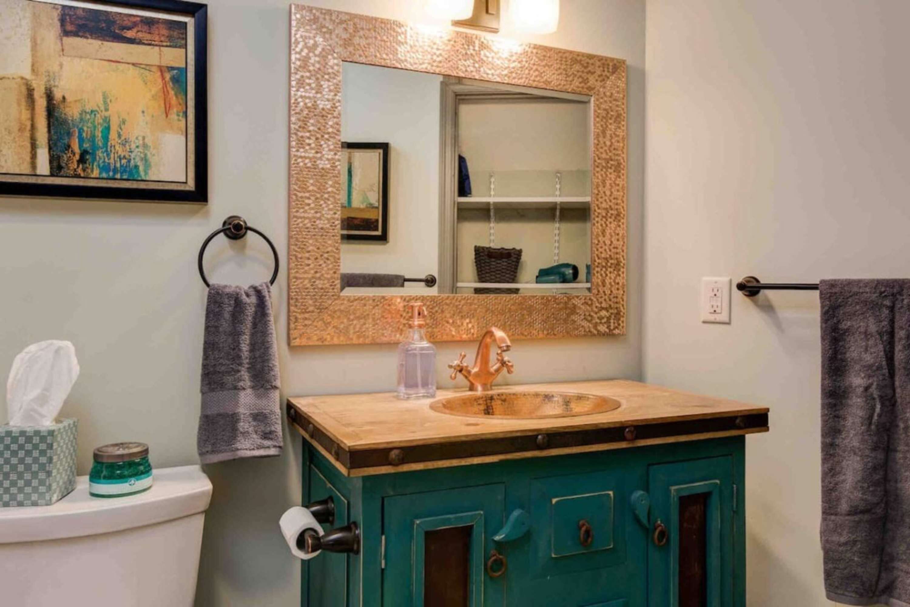A bathroom with a sink, mirror, towel rack, and a painting on the wall.