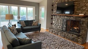 A living room with a stone fireplace, a television mounted above it, and a sofa with patterned cushions. - 550 Massive 4 Bedroom Home Sleeps 19 (Candler)